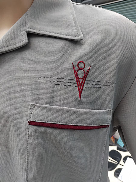 close up of grey shirt with a burgundy red embroidered v8 logo on the chest.