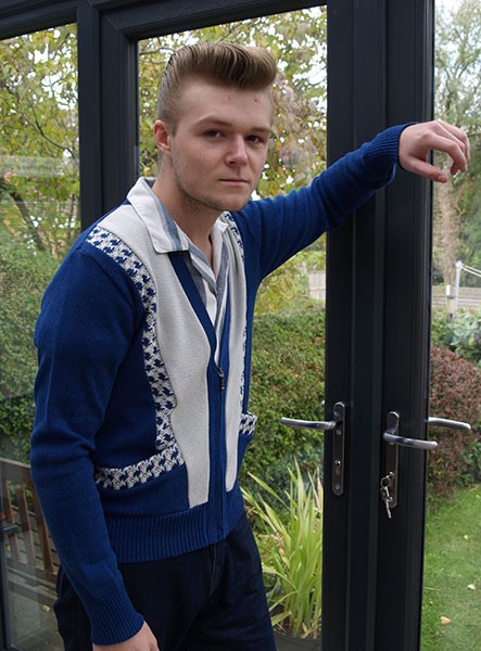 Man wearing a blue sweater with a patterned design, standing by a glass door.