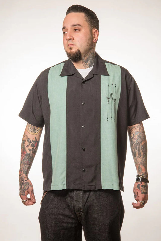 Man wearing a black and green striped shirt with tattoos on arms against a white background
