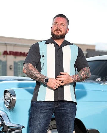 Man standing in front of a classic blue car with a building in the background