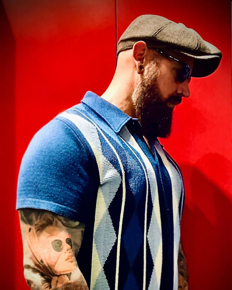 Man wearing a blue and white argyle sweater over a blue shirt against a red background