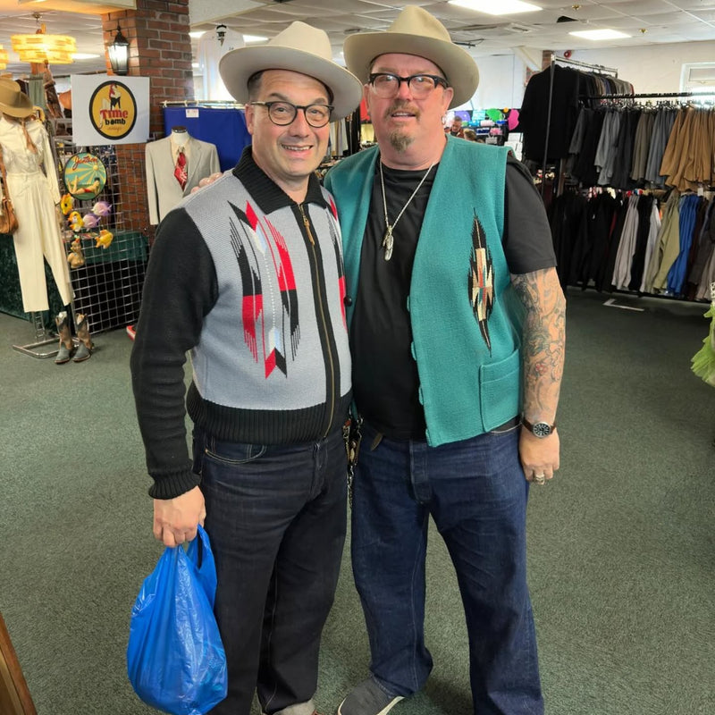 Two men wearing hats and vests standing in a store with clothing racks in the background.
