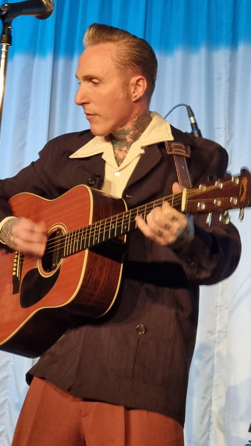 Person playing an acoustic guitar on a stage with a blue curtain background
