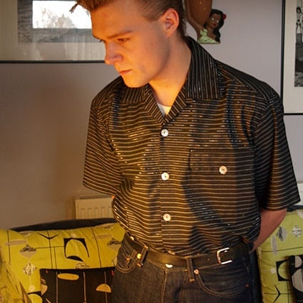 Man wearing a patterned shirt in an indoor setting with furniture and decor.